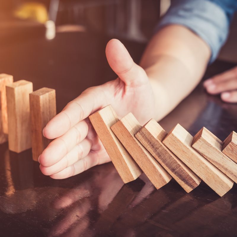 Prévention des risques financiers avec une stratégie de gestion de patrimoine, main arrêtant une chute de dominos Prévention des risques financiers avec une stratégie de gestion de patrimoine, main arrêtant une chute de dominos